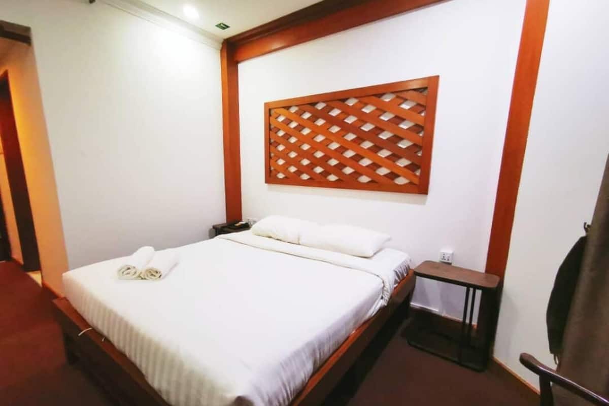 A hotel room with a bed, a wooden headboard, a nightstand, and a chair.