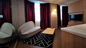 A modern hotel room with a sofa, a small table, a TV, and a wooden counter.