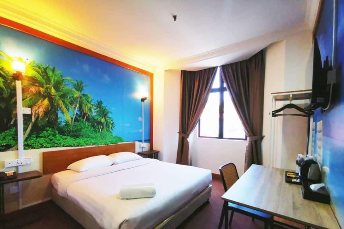 A hotel room with a bed, a desk, a chair, a TV, and a window with curtains.