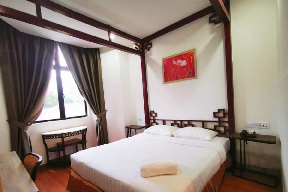 A room with a large bed, a desk, a chair, and a window with curtains.