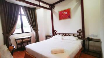A room with a large bed, a desk, a chair, and a window with curtains.
