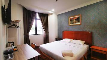 Une chambre d’hôtel avec un lit, un bureau avec une chaise, une table avec des bouteilles, un téléviseur fixé au mur et un tableau accroché au mur.