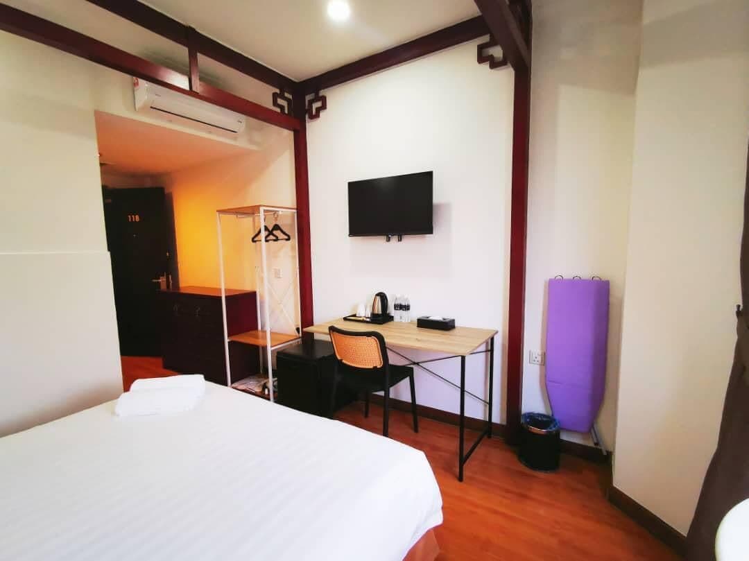 A hotel room with a bed, a desk with a chair, a television mounted on the wall, and a purple exercise mat.