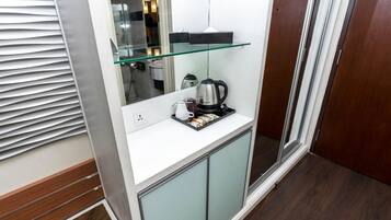 A compact kitchenette with a glass shelf, a coffee maker, and a kettle.
