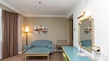 Una habitación de hotel con un sofá azul, una mesita pequeña, un escritorio con espejo y una lámpara.