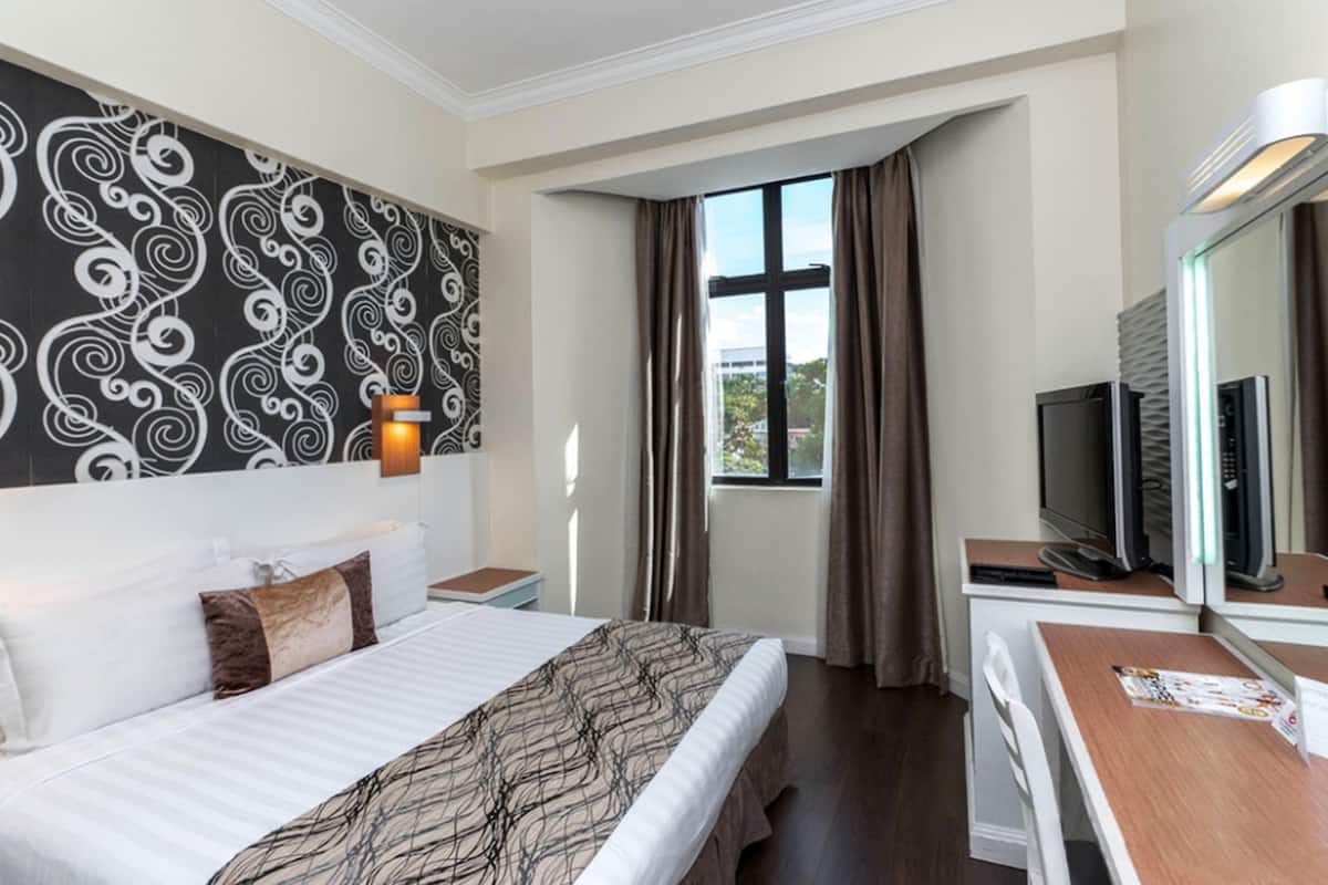 A hotel room with a large bed, a desk with a computer, a TV, and a window with curtains.