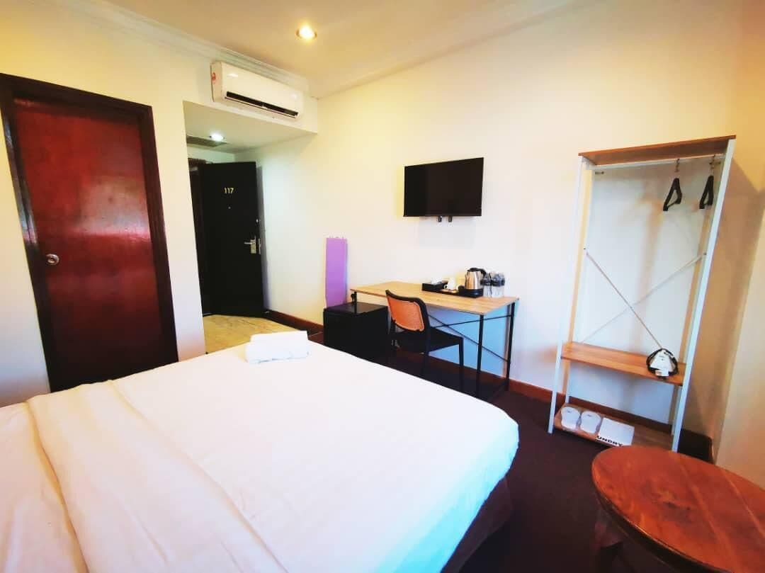 A hotel room with a bed, a desk, a chair, a wardrobe, and a TV on the wall.