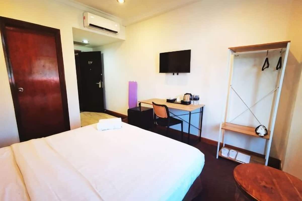 A hotel room with a bed, desk, chair, TV, and a wardrobe.