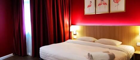 Una habitación de hotel con una cama grande, paredes rojas y tres cuadros enmarcados de flamencos.