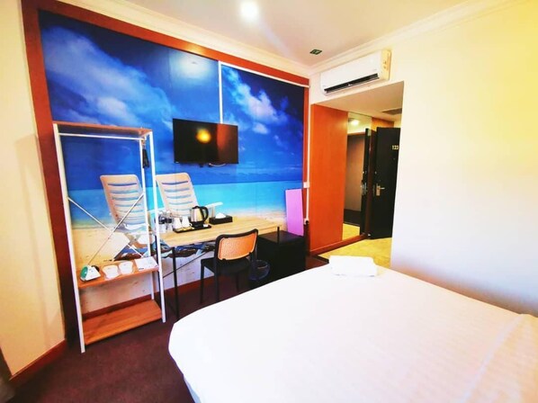 A hotel room with a bed, a desk with a chair, a TV, and a view of the beach through a large window.