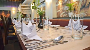A restaurant setting with neatly arranged tables, each with folded white napkins, clear glassware, and silverware.