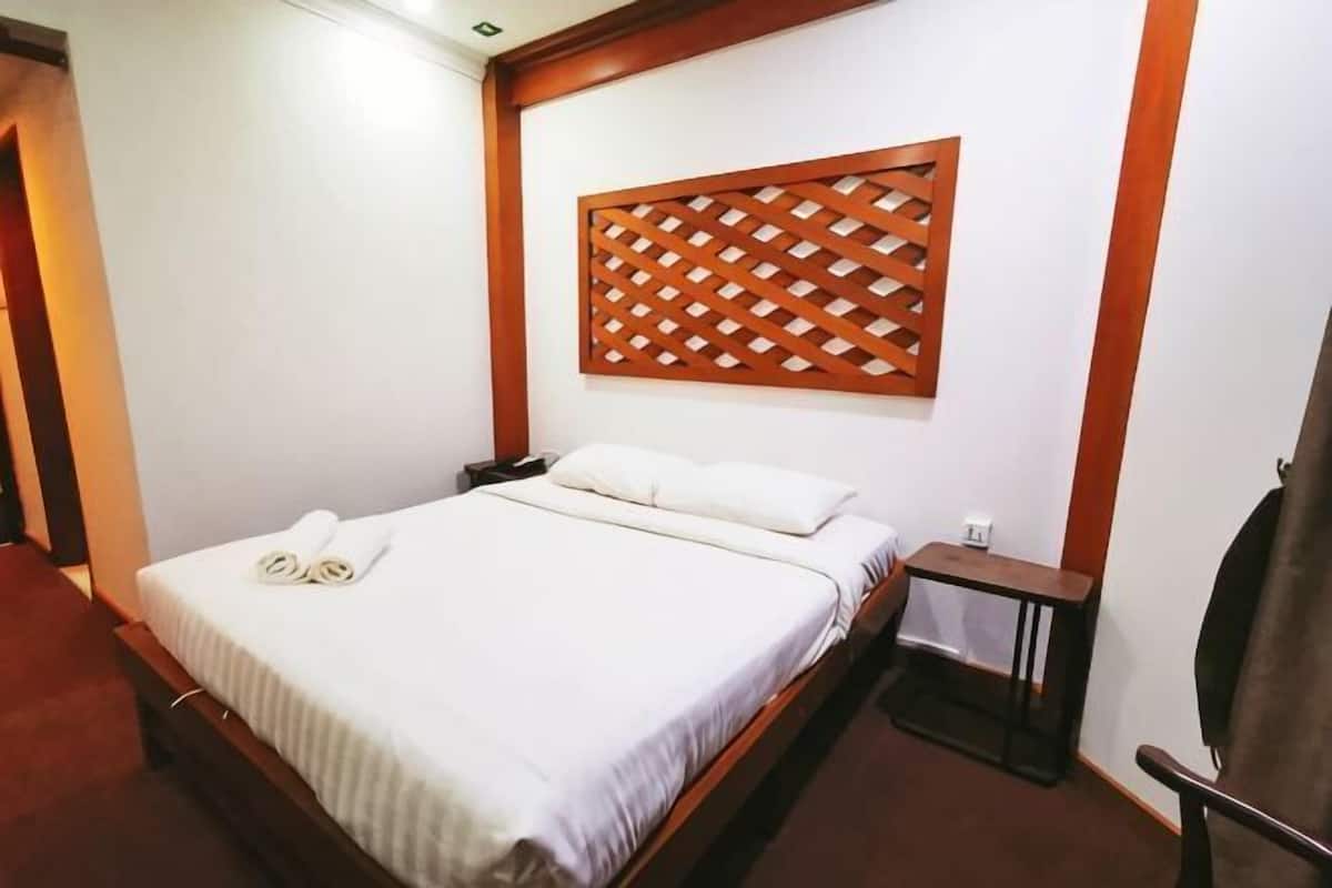 A hotel room with a bed, a wooden headboard, a nightstand, and a chair.