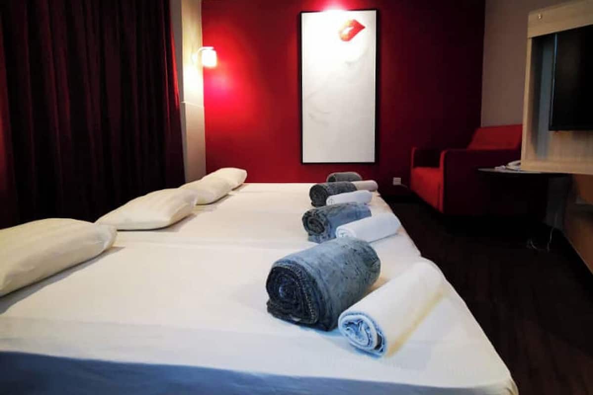 A hotel room with a large bed, red walls, and a red curtain.