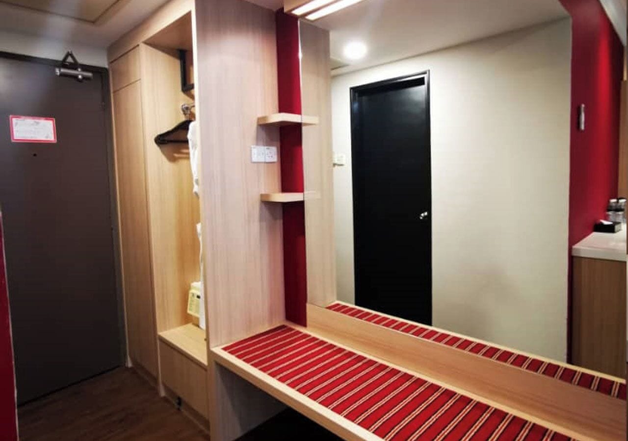 A hotel room with a wooden vanity, a mirror, a red-striped bench, and a black door.