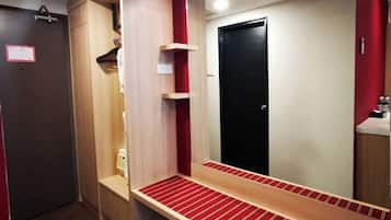 A hotel room with a wooden vanity, a mirror, a red-striped bench, and a black door.