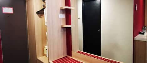 Habitación de hotel con tocador de madera, un espejo, un banco a rayas rojas y una puerta negra.