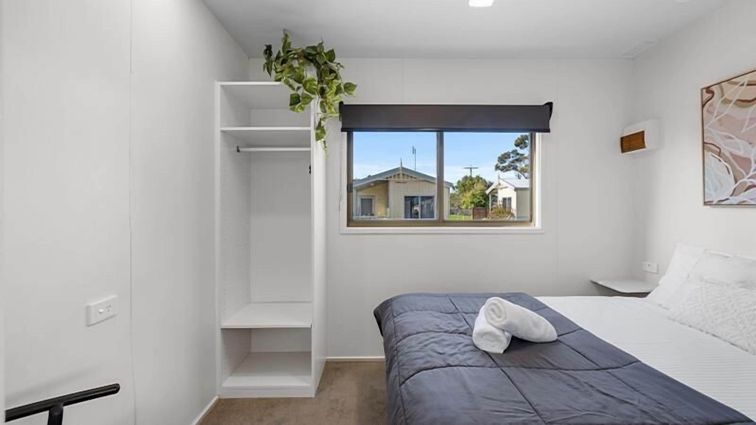 Een slaapkamer met een bed, een raam, een witte kledingkast en een plant.