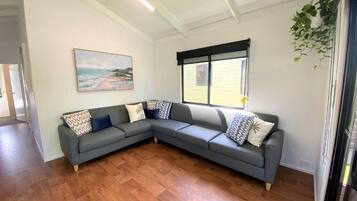 Una sala de estar moderna con un sofá seccional gris, un cuadro en la pared y un amplio ventanal con persianas.
