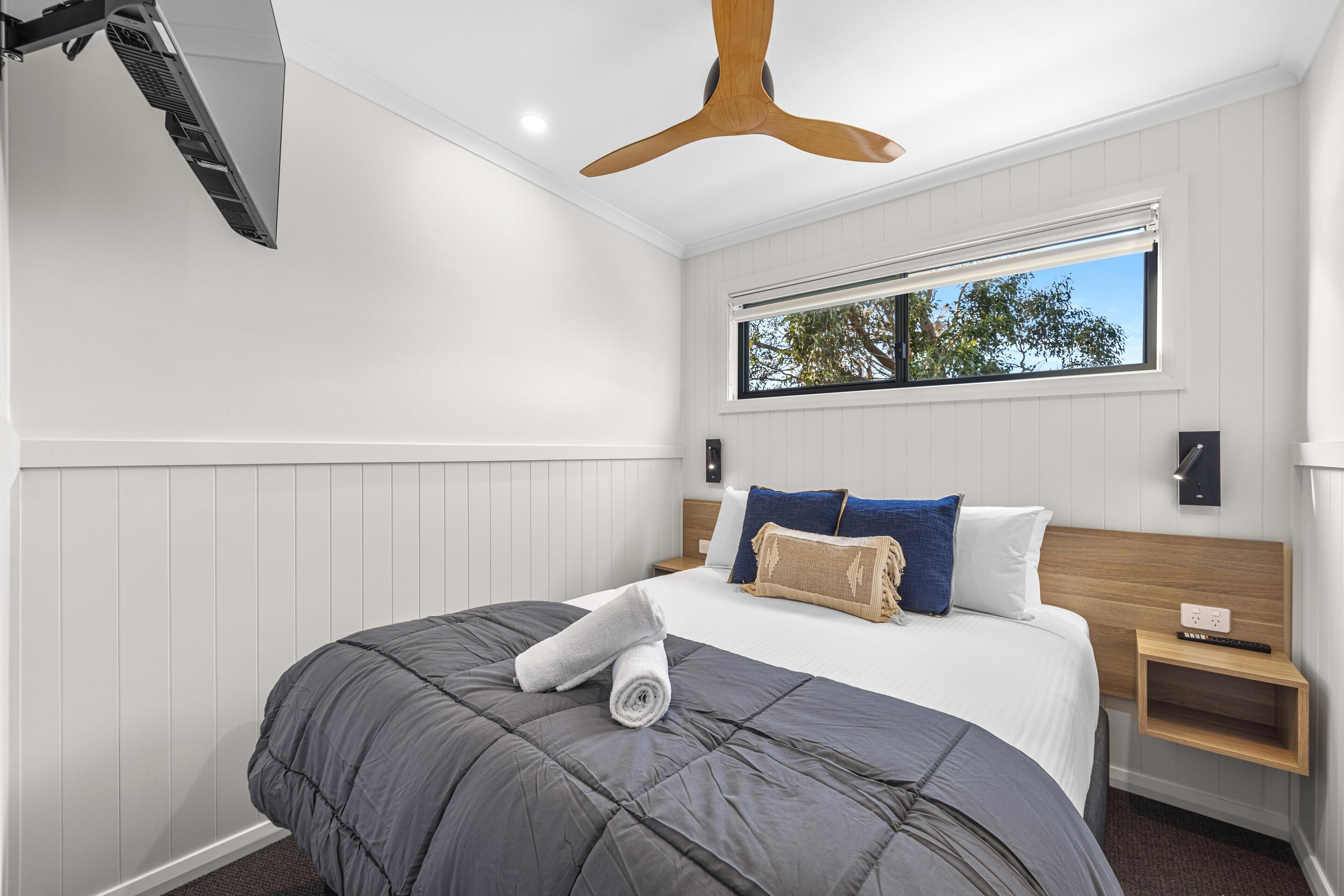 A modern hotel room with a large bed, a ceiling fan, a window with a view, and a small bedside table.