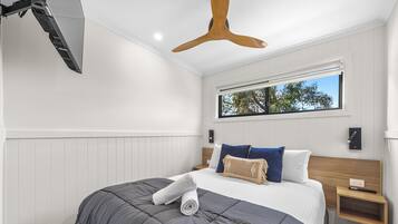 A modern hotel room with a large bed, a ceiling fan, a window with a view, and a small bedside table.