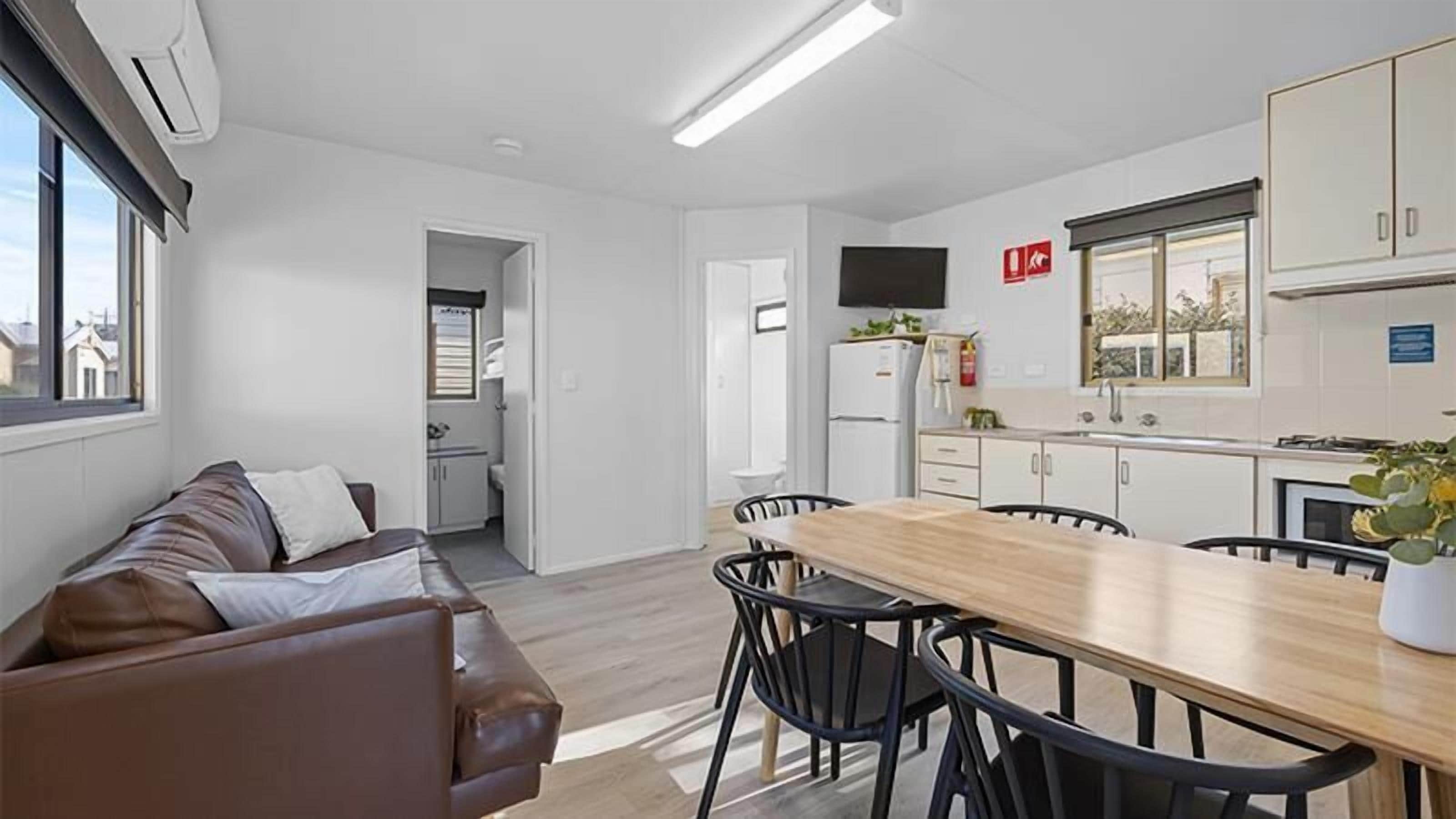 A modern kitchen with a dining area, a sofa, and a TV mounted on the wall.