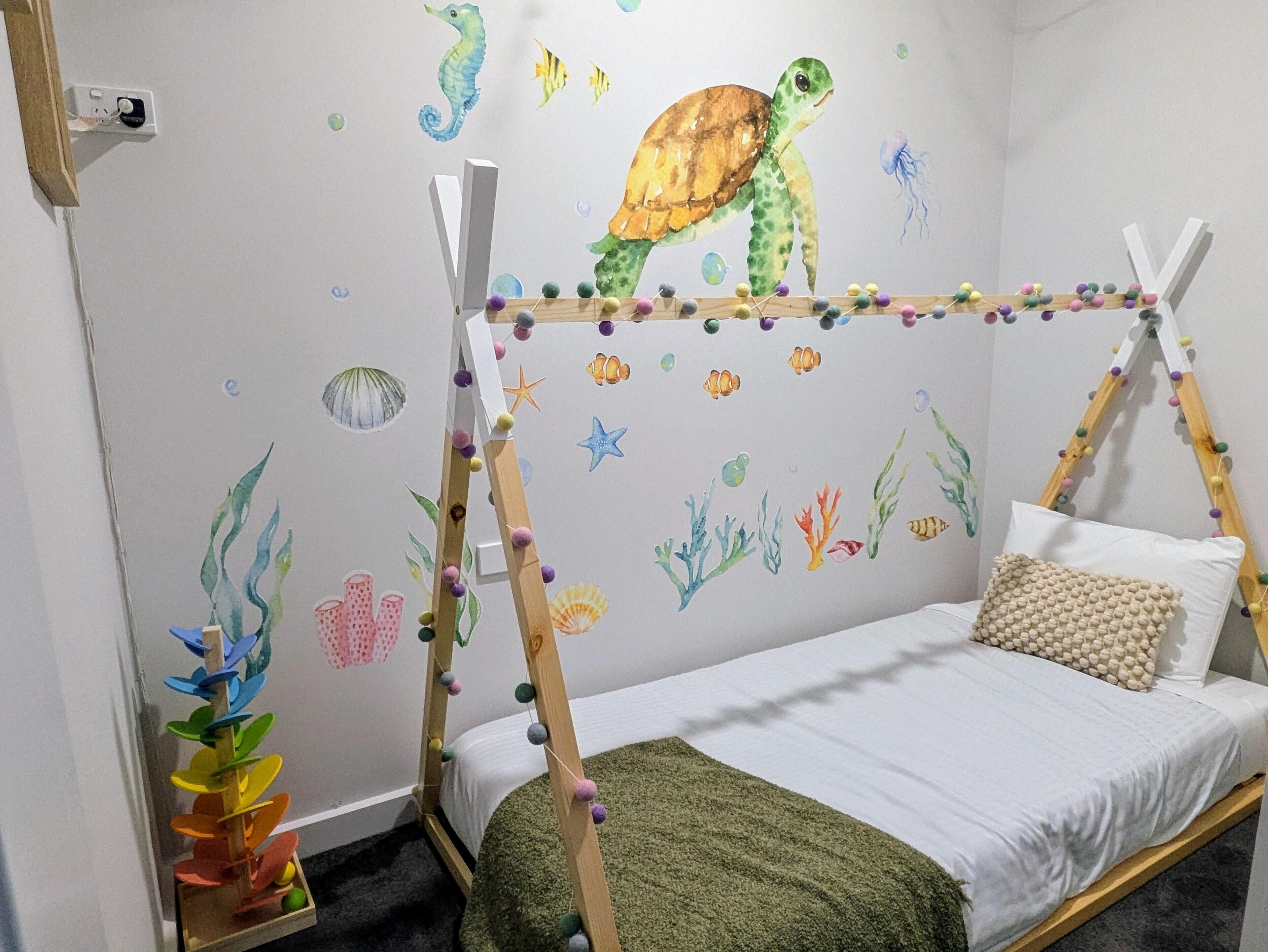 Een kinderkamer met een bed, een houten trap en een muur beschilderd met zeedieren.