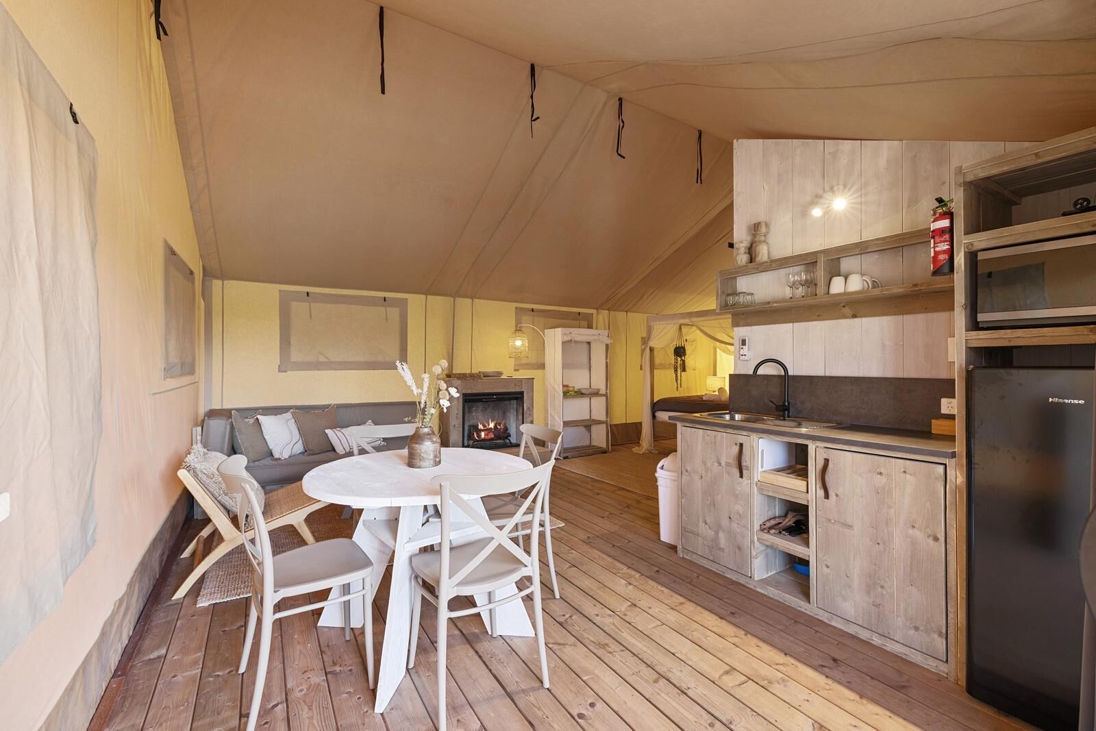 A cozy room with a round dining table, white chairs, a sofa, a fireplace, and a kitchenette with a refrigerator.