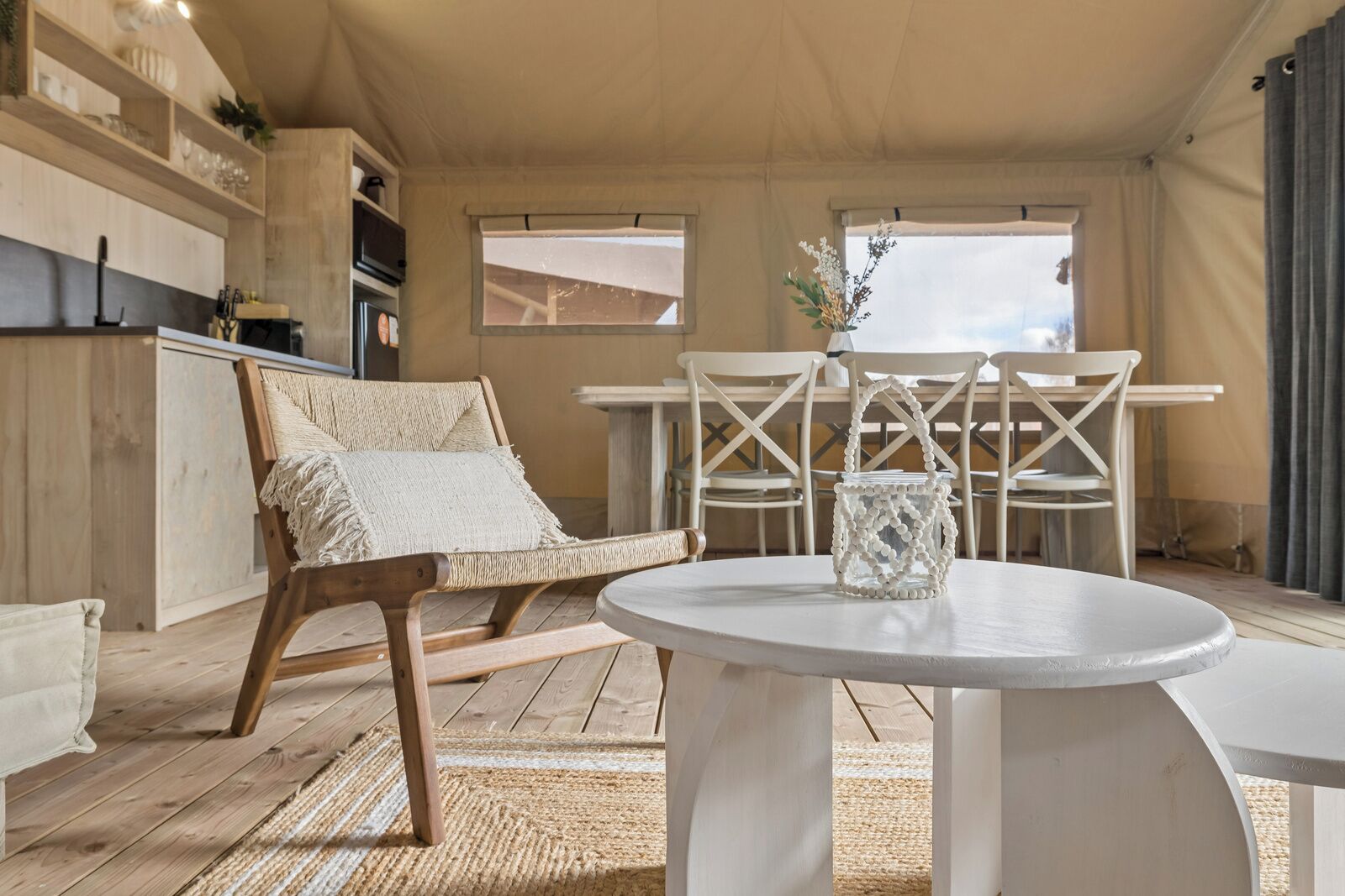 Una habitación acogedora con piso de madera, una mesa redonda blanca, una silla de mimbre y una lámpara blanca.