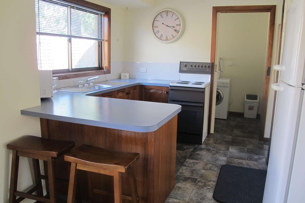 A compact kitchen with a central island, wooden stools, a stove, and a clock on the wall.