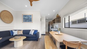 Uma sala de estar moderna com um sofá azul escuro, uma mesa de centro de madeira e uma mesa de jantar de madeira com um banco.