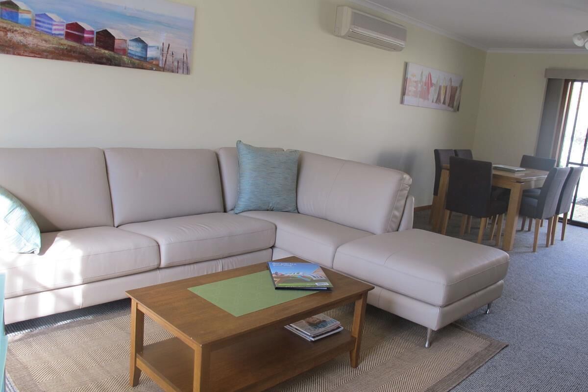 A living room with a beige sofa, a wooden coffee table, and a dining area with chairs and a table.