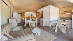Um quarto espaçoso com uma cama grande, um espaço de estar com sofá e poltronas, uma pequena mesa de jantar e uma cozinha.