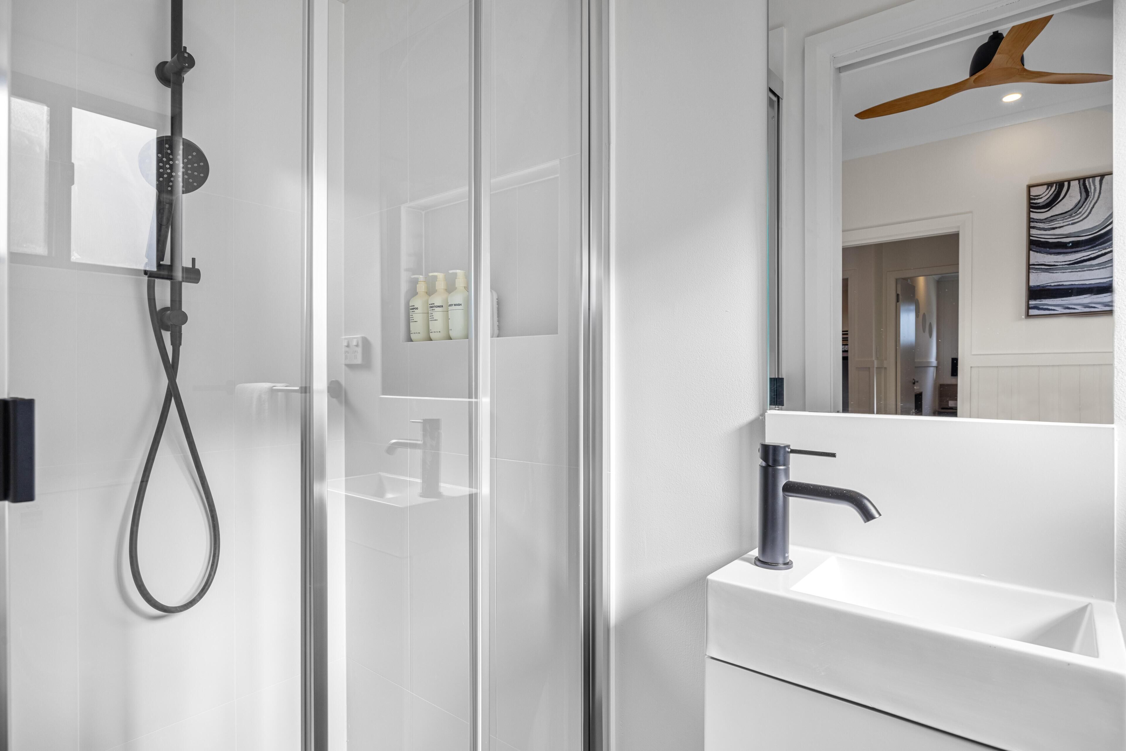 Un baño moderno con cabina de ducha de vidrio, un lavamanos blanco y un ventilador de techo de madera.