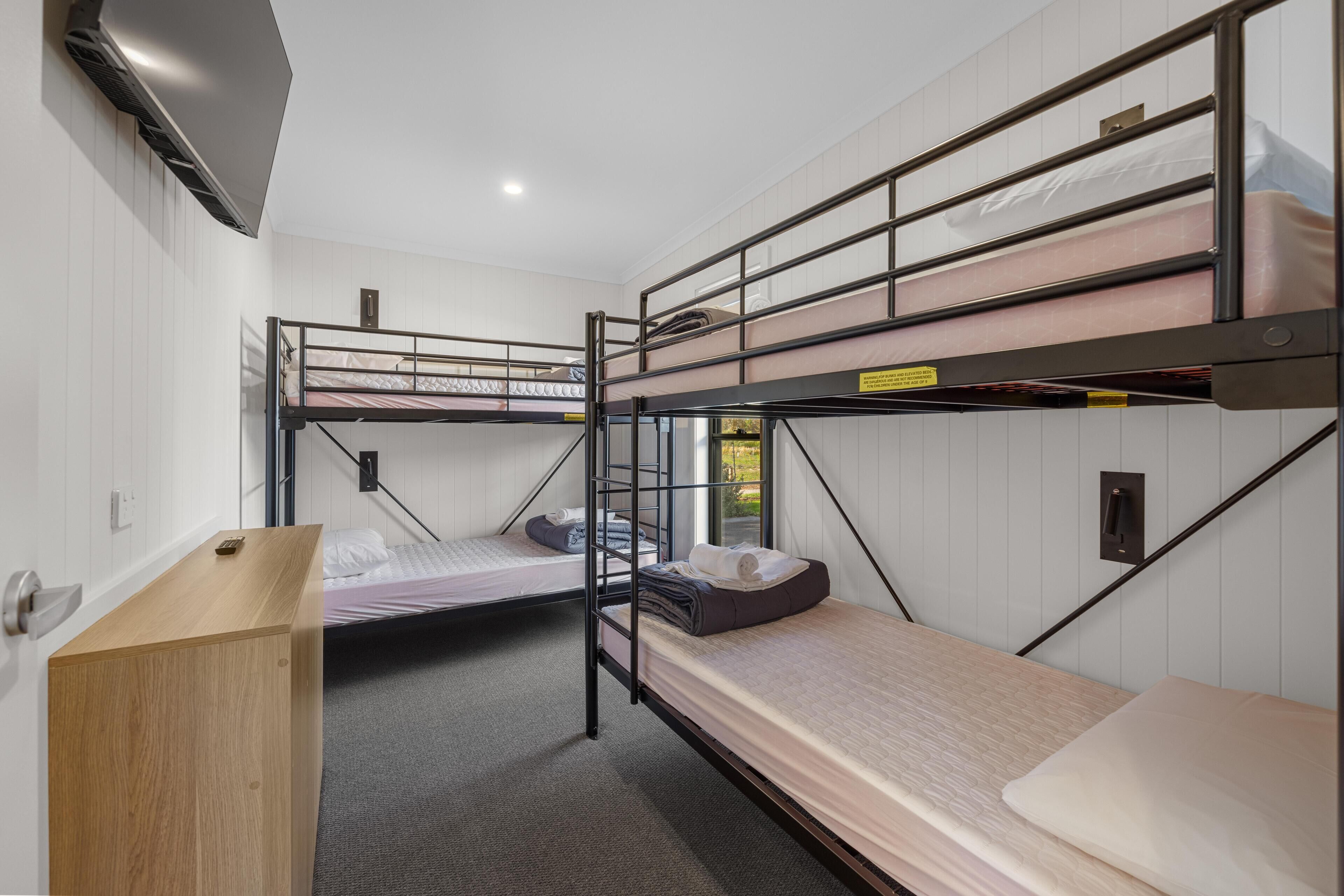 A bunk bed room with a wooden desk, white walls, and a window.
