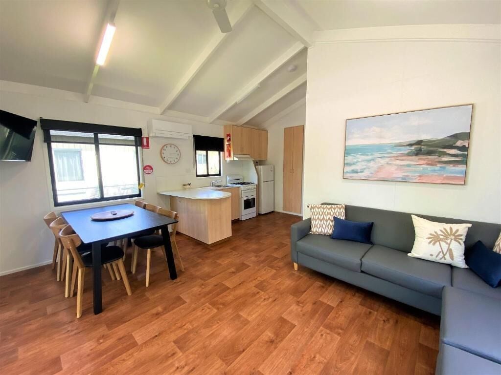 Un espace de vie compact comprenant un coin repas, une kitchenette et un canapé agrémenté de coussins décoratifs.