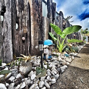 A rustic outdoor area with a wooden fence, a statue of a child holding a surfboard, and various plants. - A Raceview Motor Inn (Newtown)