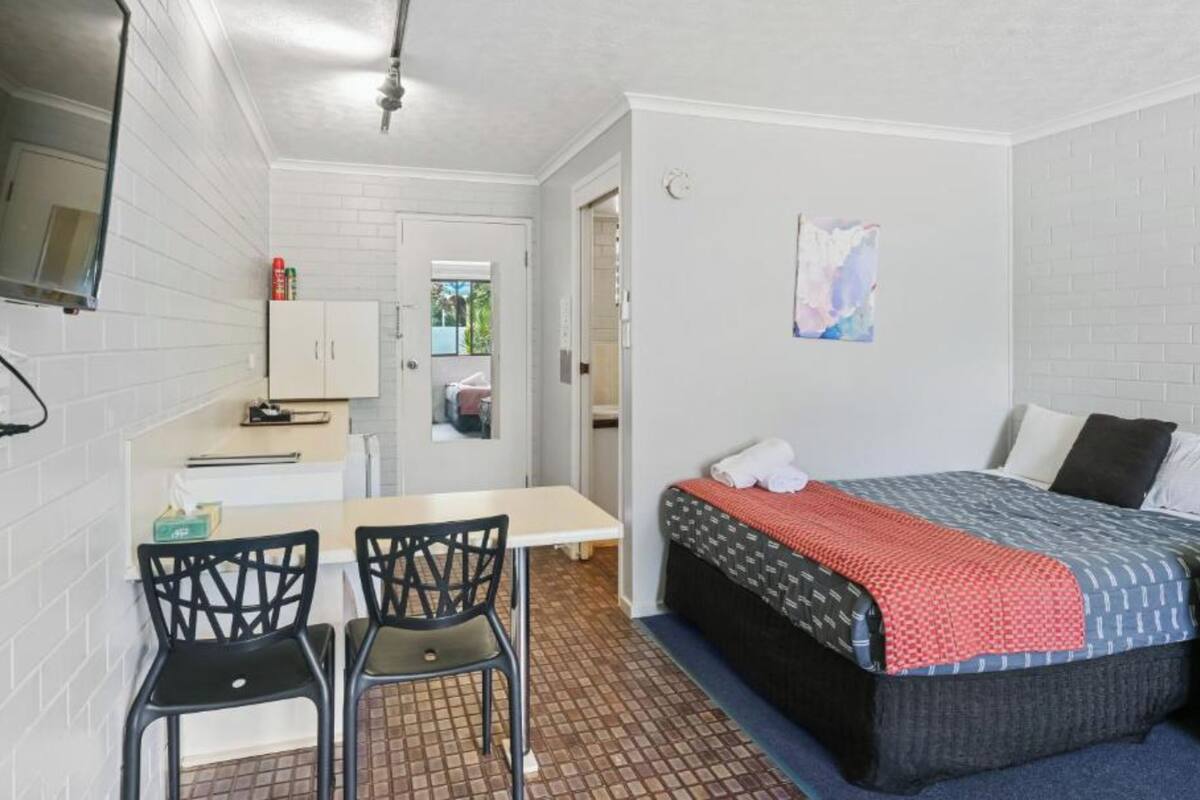 A compact room with a bed, a small desk with a chair, and a television mounted on the wall.