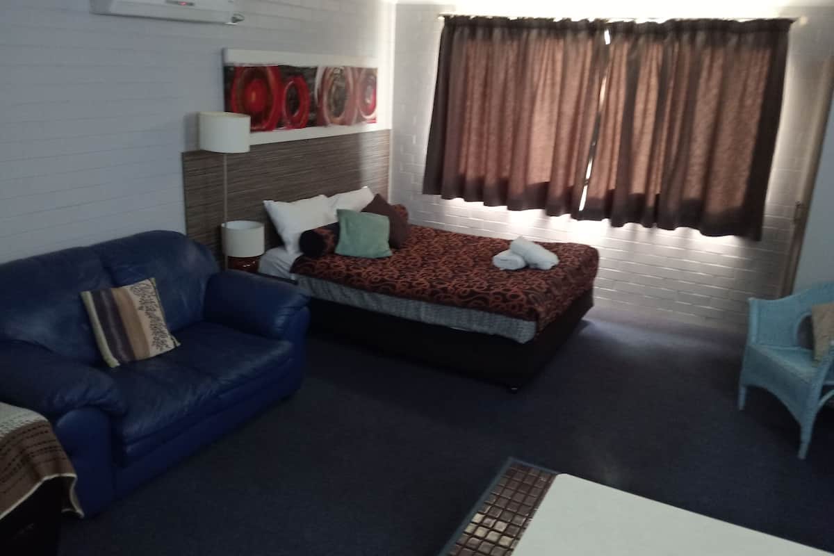 A hotel room with a bed, a blue sofa, a small table, and a window with curtains.