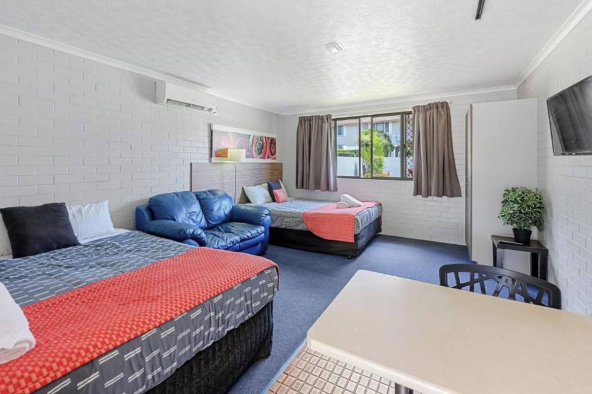 A compact room with two beds, a sofa, a table, and a window with curtains.