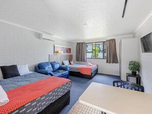 A compact room with two beds, a sofa, a table, and a window with curtains.