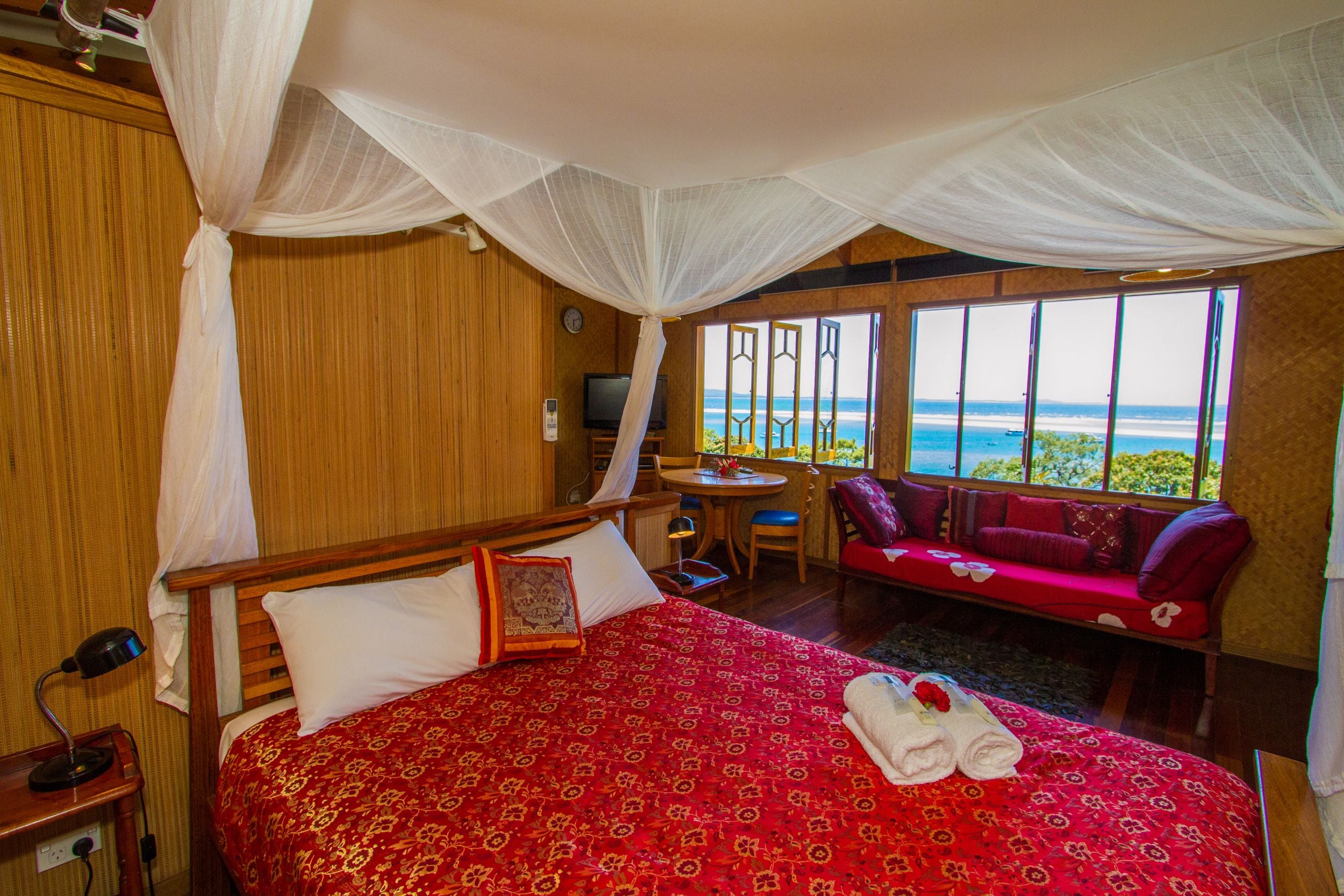 A hotel room with a large bed, a TV, a small table, and a sofa with a view of the ocean.