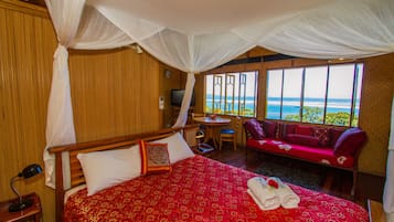 A hotel room with a large bed, a TV, a small table, and a sofa with a view of the ocean.