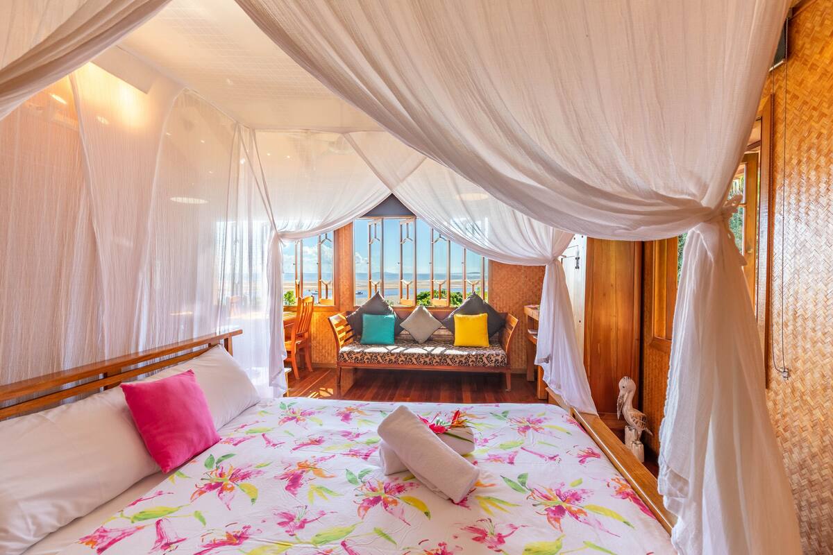 Una habitación con cama, un banco con cojines y vista al mar.