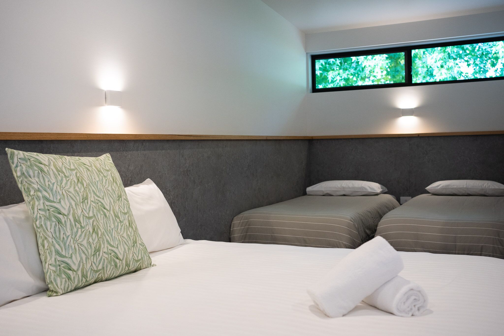 Une chambre d’hôtel avec deux lits simples, un grand lit avec une serviette roulée et une fenêtre donnant sur un paysage verdoyant.