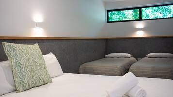 Une chambre d’hôtel avec deux lits simples, un grand lit avec une serviette roulée et une fenêtre donnant sur un paysage verdoyant.
