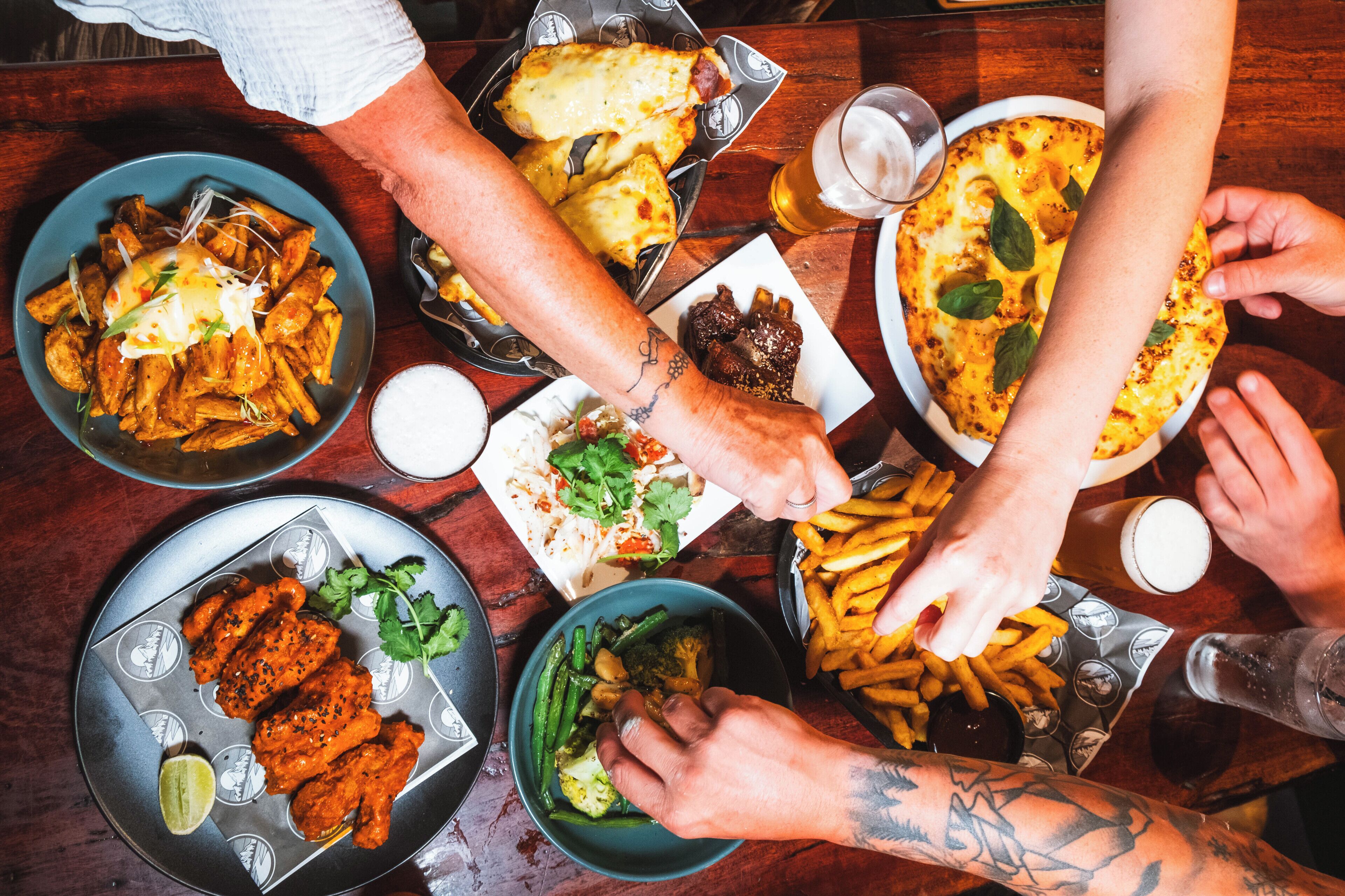 Un gruppo di persone sedute a un tavolo con diversi piatti, tra cui patatine fritte, alette di pollo e una pizza.