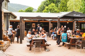 An outdoor seating area with wooden tables and benches, surrounded by a rustic building with a mountain backdrop. - Harrietville Hotel Motel (Harrietville)