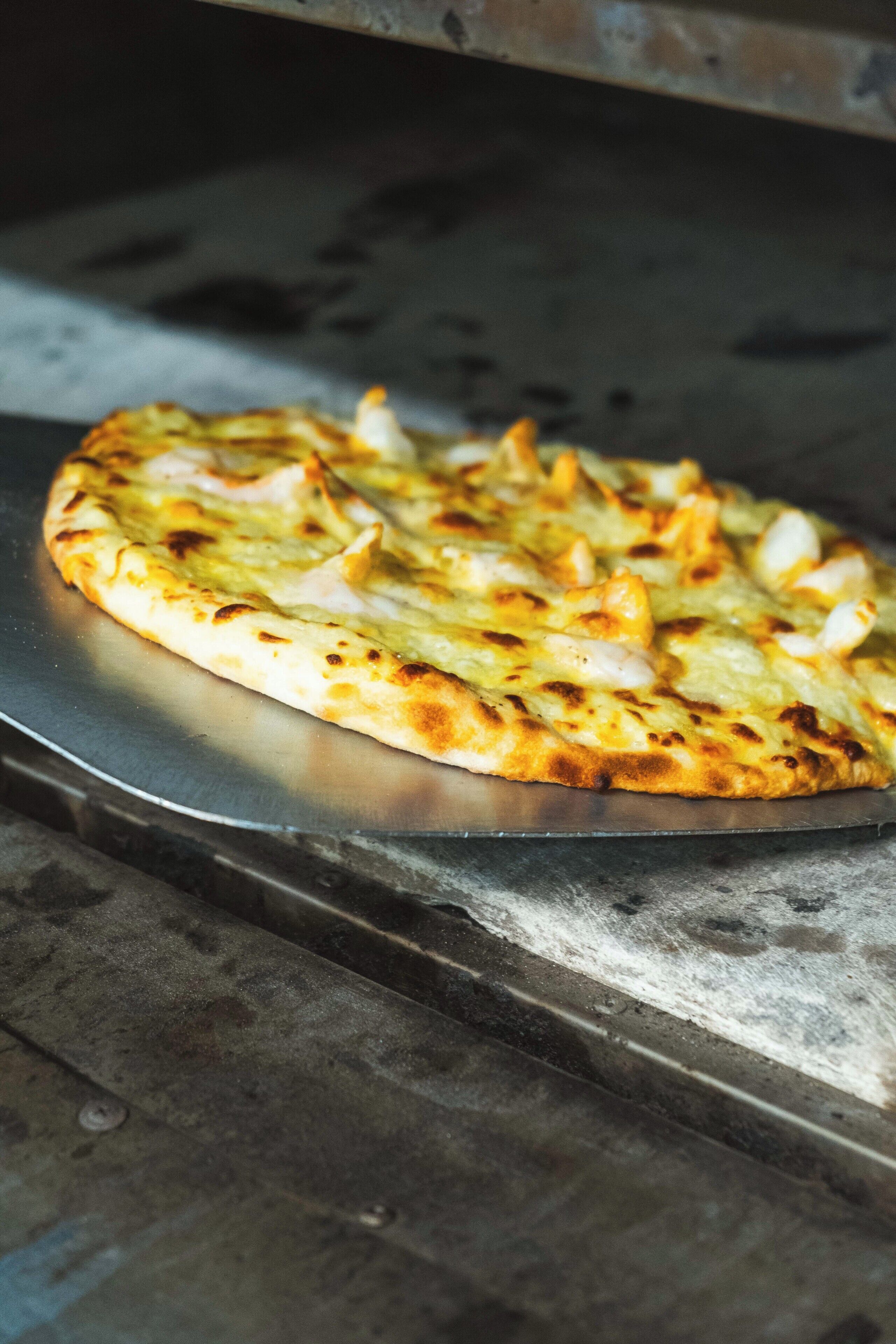 Una pizza sobre una bandeja metálica en una cocina.