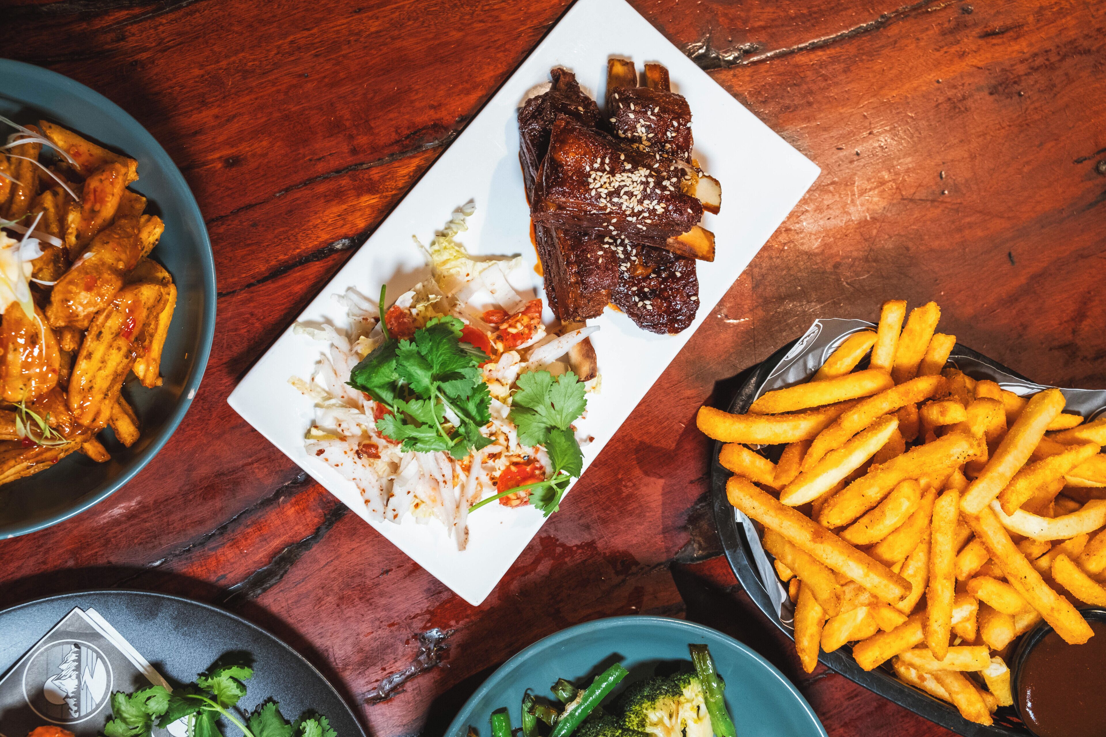 Un plato con costillas, papas fritas y una ensalada como acompañamiento sobre una mesa de madera.