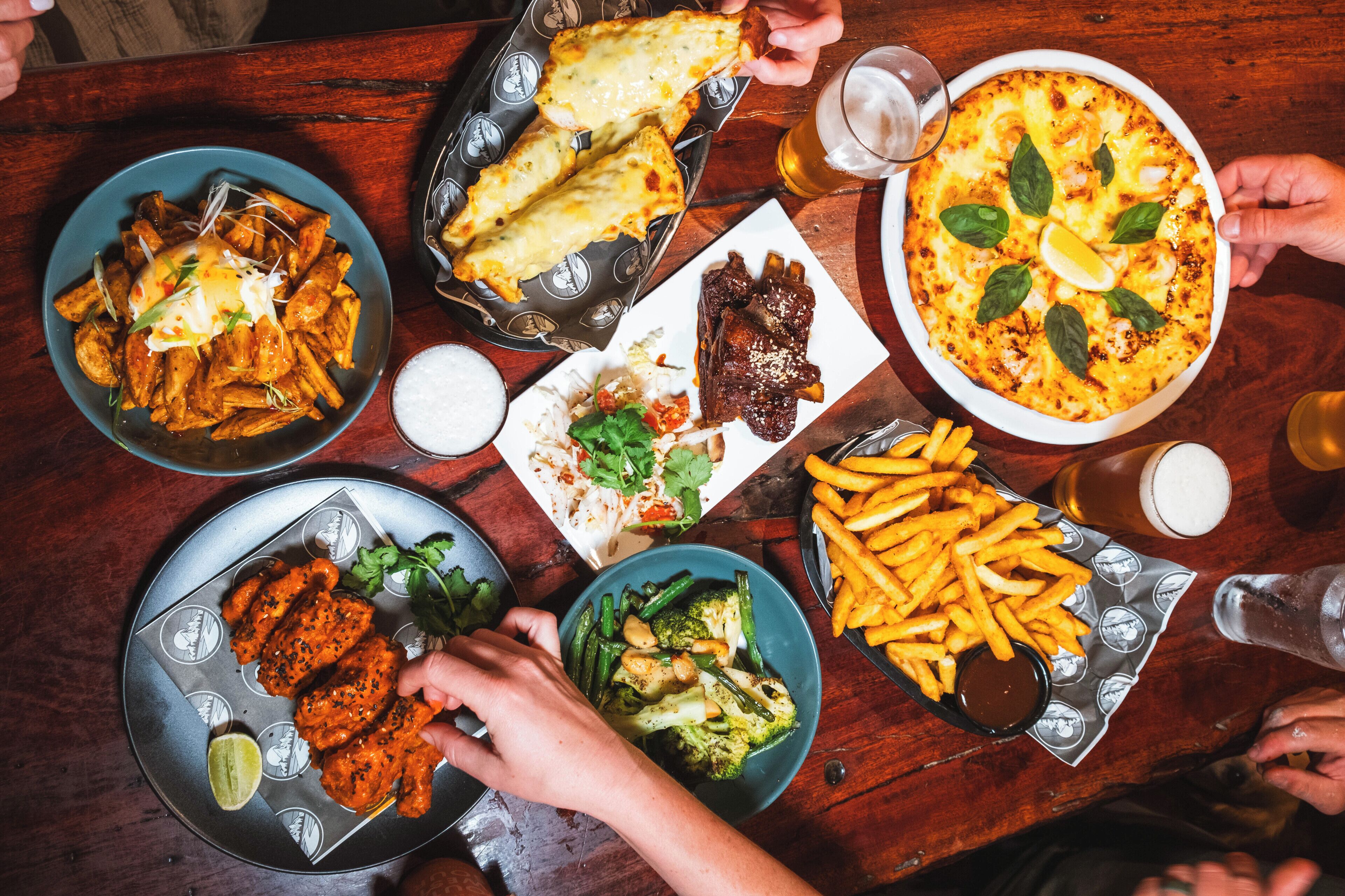 Diversos pratos sobre uma mesa, incluindo batatas fritas, pizza e carnes.